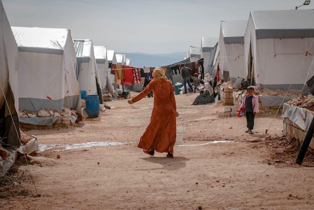 Back view of anonymous Muslim female in traditional clothes walking on dirty path near camps in refugee camp